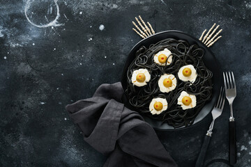 Halloween party Italian black pasta decorated horror olives like eyes on black plate on old dark...