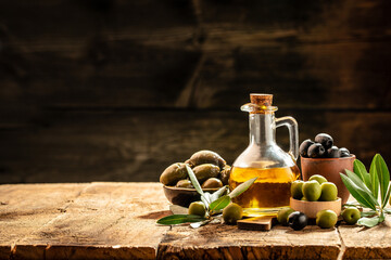 Obraz na płótnie Canvas Olive oil in bottles with black and green olives and leaves. extra virgin olive oil jars on a wooden background. place for text