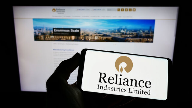 Stuttgart, Germany - 09-22-2022: Person holding mobile phone with logo of Indian company Reliance Industries Limited on screen in front of web page. Focus on phone display.