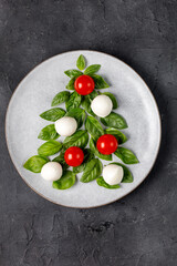 Caprese salad in the form of a Christmas tree. Festive tomato mozzarella and basil appetizer on light plate.