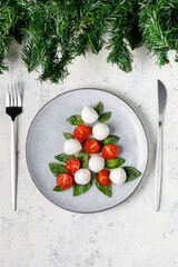 Caprese salad in the form of a Christmas tree. Festive tomato mozzarella and basil appetizer on light plate.