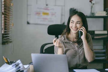 Obraz premium Portrait of a beautiful Asian woman looking at laptop screen while sitting at working desk in the office