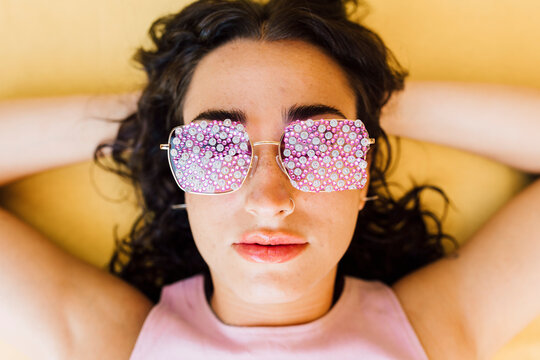 Woman Wearing Psychedelic Sunglasses Lying Over Yellow Background