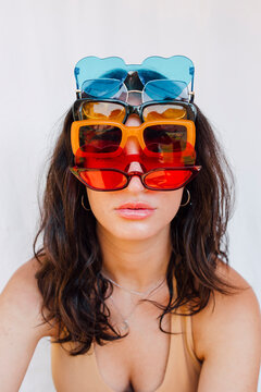 Young woman wearing various sunglasses in front of white wall