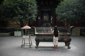 chinese girl in traditional silk flower dress burning incense in temple