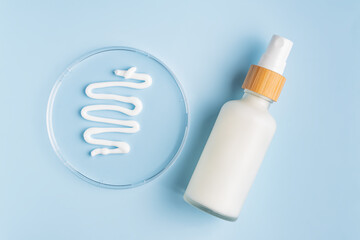 matte glass bottle with face cream fluid on blue background. Skin care cosmetics swatch in lab patri dish. Organic cosmetic product research