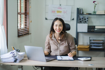 Portrait of a beautiful Asian woman looking at laptop screen while sitting at working desk in the office