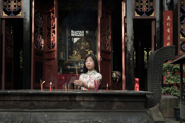chinese girl in traditional silk flower dress burning incense in temple