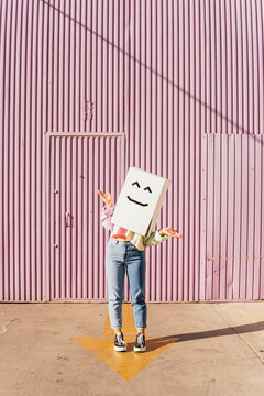 Woman wearing box with robot face gesturing in front of corrugated wall