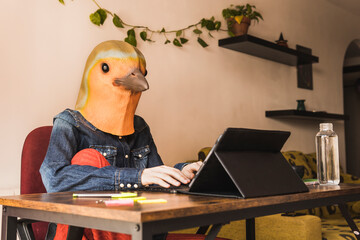 Freelancer wearing bird mask using tablet PC sitting at home