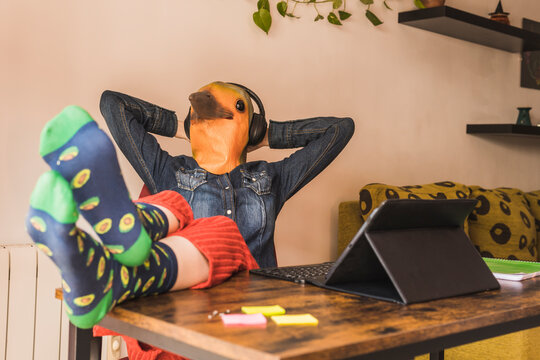 Businesswoman wearing bird mask listening to music through wireless headphones at home