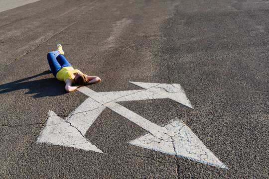Woman lying down with hands behind head near three way direction arrow sign on road