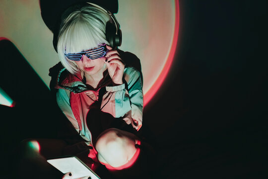 Woman adjusting neon glasses using smart phone against illuminated black background