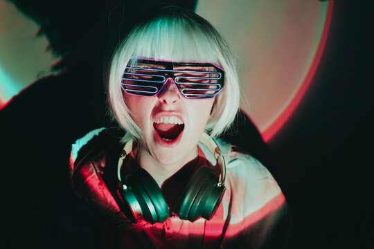 Cheerful woman with neon eyeglasses shouting against black background