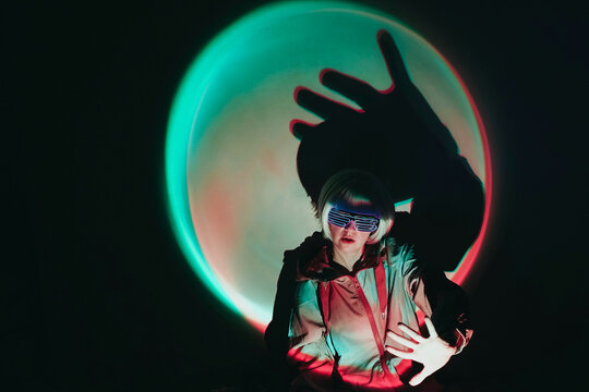 Woman wearing neon eyeglasses gesturing against black background