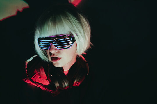 Woman with white short hair wearing neon glasses against black background