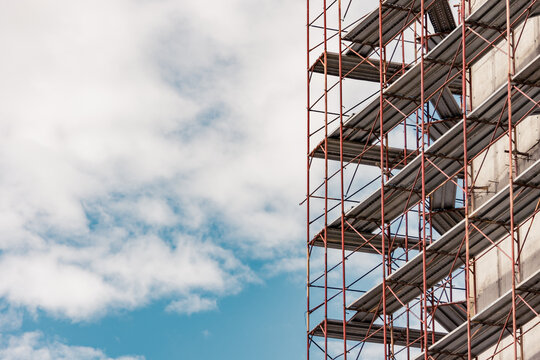Extended scaffolding at the corner of a construction site building against a cloudy sky. Metallic structure to sustain workers weight while working