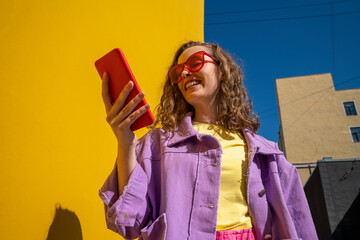 Happy woman text messaging through smart phone near wall on sunny day
