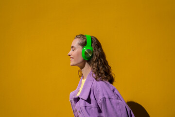 Smiling woman with headphones listening to music in front of yellow wall