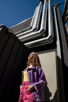 Woman with hands in pockets standing near building on sunny day