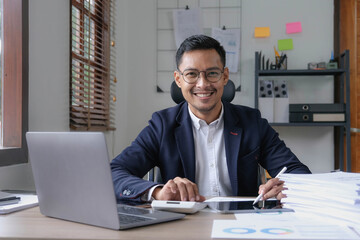 Fototapeta premium Portrait of a male business owner showing a happy smiling face as he has successfully invested his business using computers and financial budget documents at work.