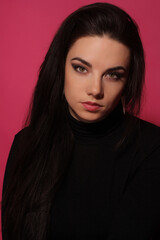 Fototapeta premium Portrait of a beautiful fashion glamour girl brunette in black clothes in the studio with big earrings on the pink background