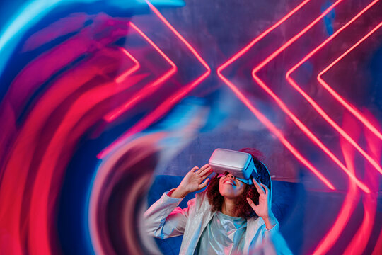 Smiling Woman With VR Glasses In Front Of Neon Light Seen Through Glass