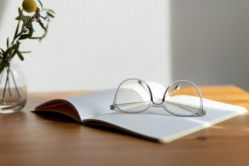 business background. glasses and notebooks are white and grey. notebook in a cage on a beautiful wooden table. Close-up with a blurred background.