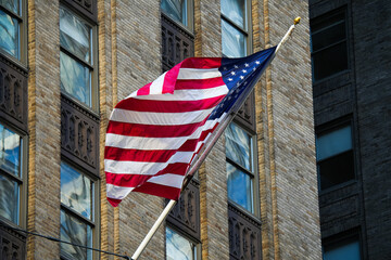 Fototapeta premium National flag of the United States of America winding in the balcony of an old skyscraper concrete brick building from New York