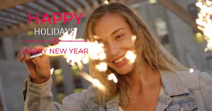 Animation of happy holidays and new year text over smiling caucasian woman holding sparklers