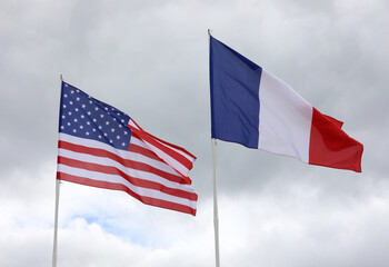 American and French flags with blue sky background waving together
