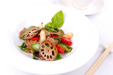 Tenderloin with vegetables and lotus root, fried in a wok. Oriental dish in a white plate, on a white background.