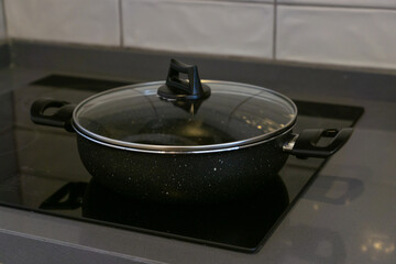 Frying pan with glass lid on the glass-ceramic hob of a kitchen.