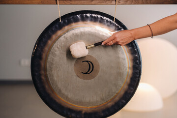 Close-up of a woman's hand pounding a gong with a hammer. Gong and hand beater for gong - obrazy, fototapety, plakaty