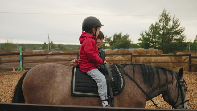 toddler is riding horse at first time in pony club, coach woman is holding baby in saddle, helping him