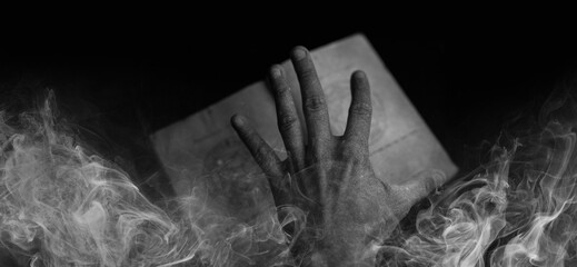 A scary hand over magic book on dark background. Mysterious composition. Fortune teller, mind...