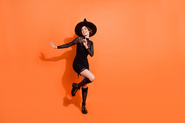 Fototapeta na wymiar Full size photo of nice young woman dance look empty space dressed trendy black halloween witch garment isolated on orange color background