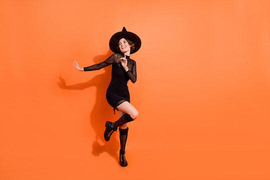 Full size photo of nice young woman dance look empty space dressed trendy black halloween witch garment isolated on orange color background