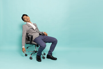 Young Asian businessman exhausted and frustrated sitting on chair office isolated on green background, Feeling failed and tired concept