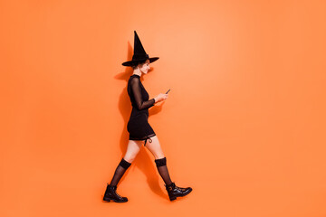 Full length profile photo of magician person walking hold use telephone isolated on orange color background