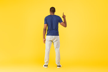 Fototapeta na wymiar Back View Of Black Guy Pointing Finger Upward, Yellow Background