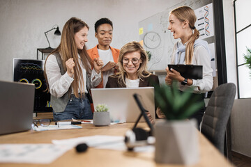 Close up of confident multiethnic businesswomen with senior female leader, working together in office, using laptop and tablet pc, discussing business strategy or new startup