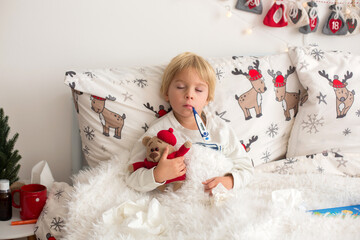 Beautiful blond toddler child, sick boy with fever, lying in bed on Christmas