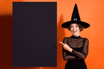 Photo of surprised cheerful sorcerer lady direct finger empty space poster isolated on orange color background - obrazy, fototapety, plakaty