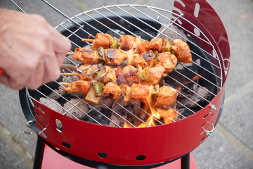 man flipping chicken skewers on barbecue grill over hot coals, summer delicacies