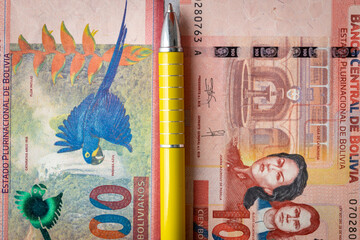financial settlements in Bolivia, concept, Two 100 Bolivares banknotes stacked next to each other, a yellow pen between them, taxes in Bolivia, close-up, top view