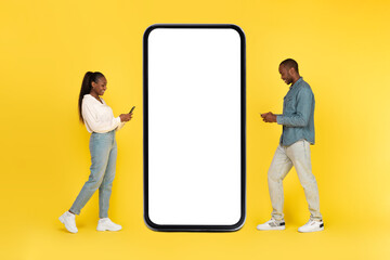 African Couple Using Phones Posing Near Large Cellphone, Yellow Background