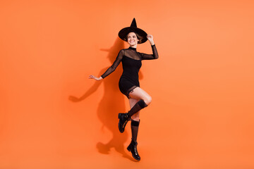 Fototapeta na wymiar Full length photo of charming lady jumping look empty space dressed trendy black halloween garment isolated on orange color background