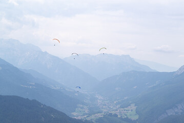 Fototapeta na wymiar A group of four paragliders flying over valley surrounded of mountain on a cloudy day at french alps.