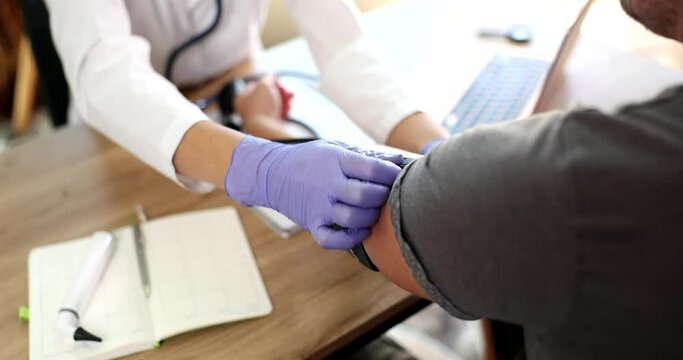 Doctor puts cuff of blood pressure monitor on outstretched arm of patient